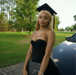 AyeitsMaya holding her graduation degree next to her car